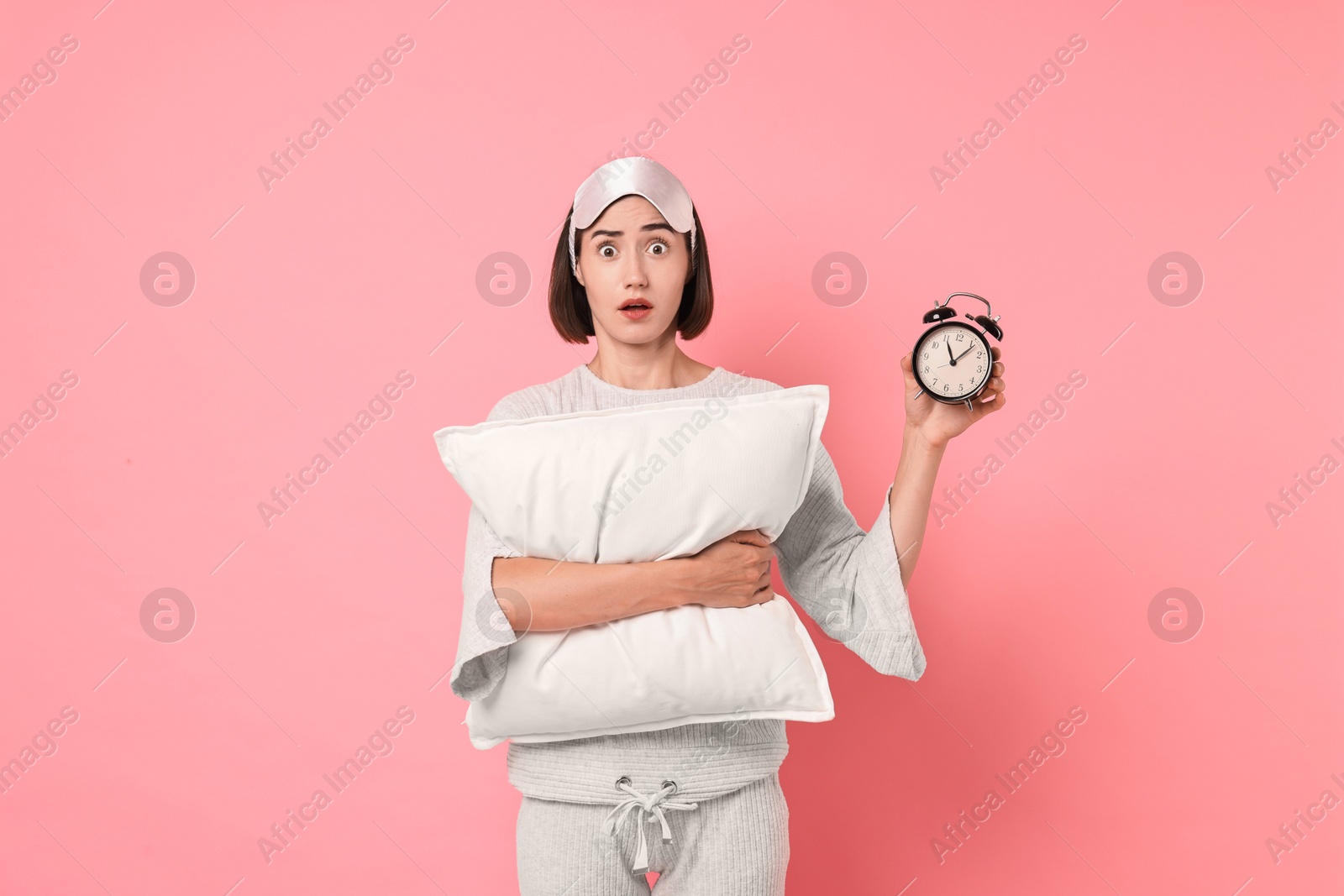 Photo of Overslept young woman with sleep mask, pillow and alarm clock on pink background