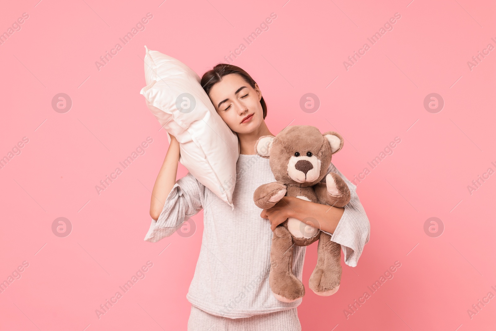 Photo of Overslept young woman with teddy bear and pillow on pink background