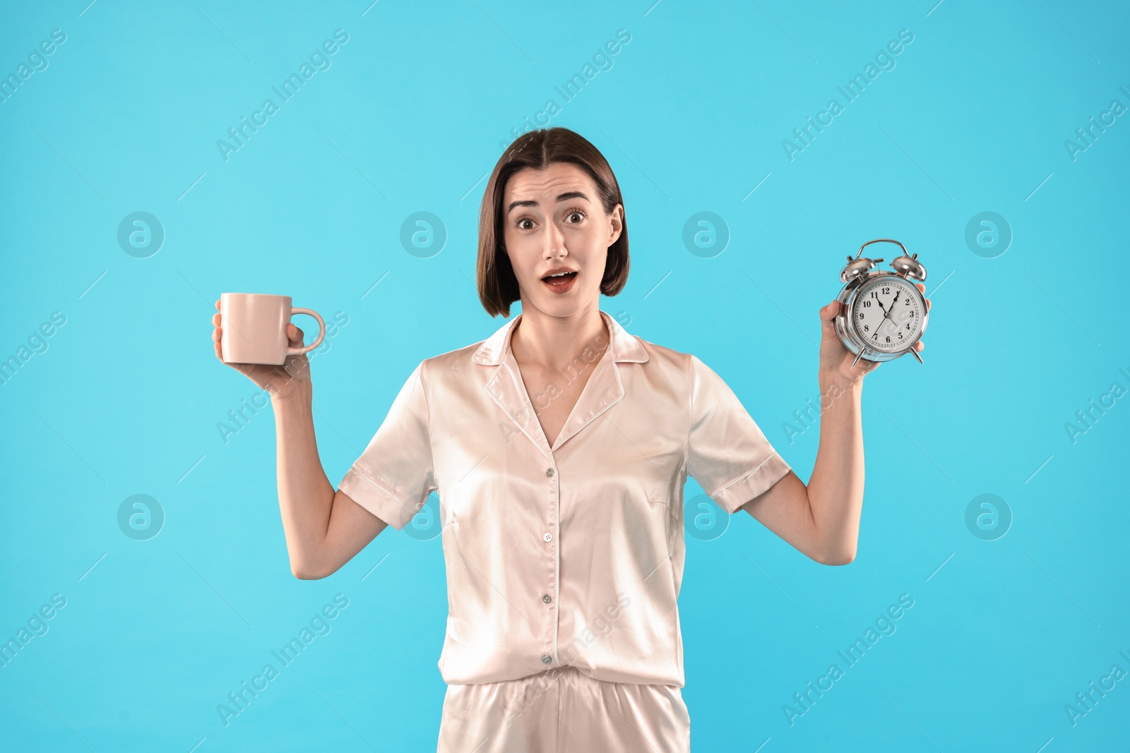 Photo of Overslept young woman with cup and alarm clock on light blue background