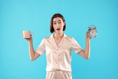 Photo of Overslept young woman with cup and alarm clock on light blue background