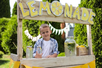 Photo of Cute little boy with refreshing drink at lemonade stand in park