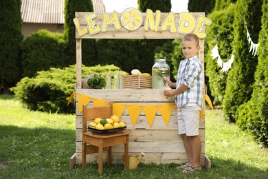 Photo of Cute boy pouring refreshing lemonade into paper cup in park