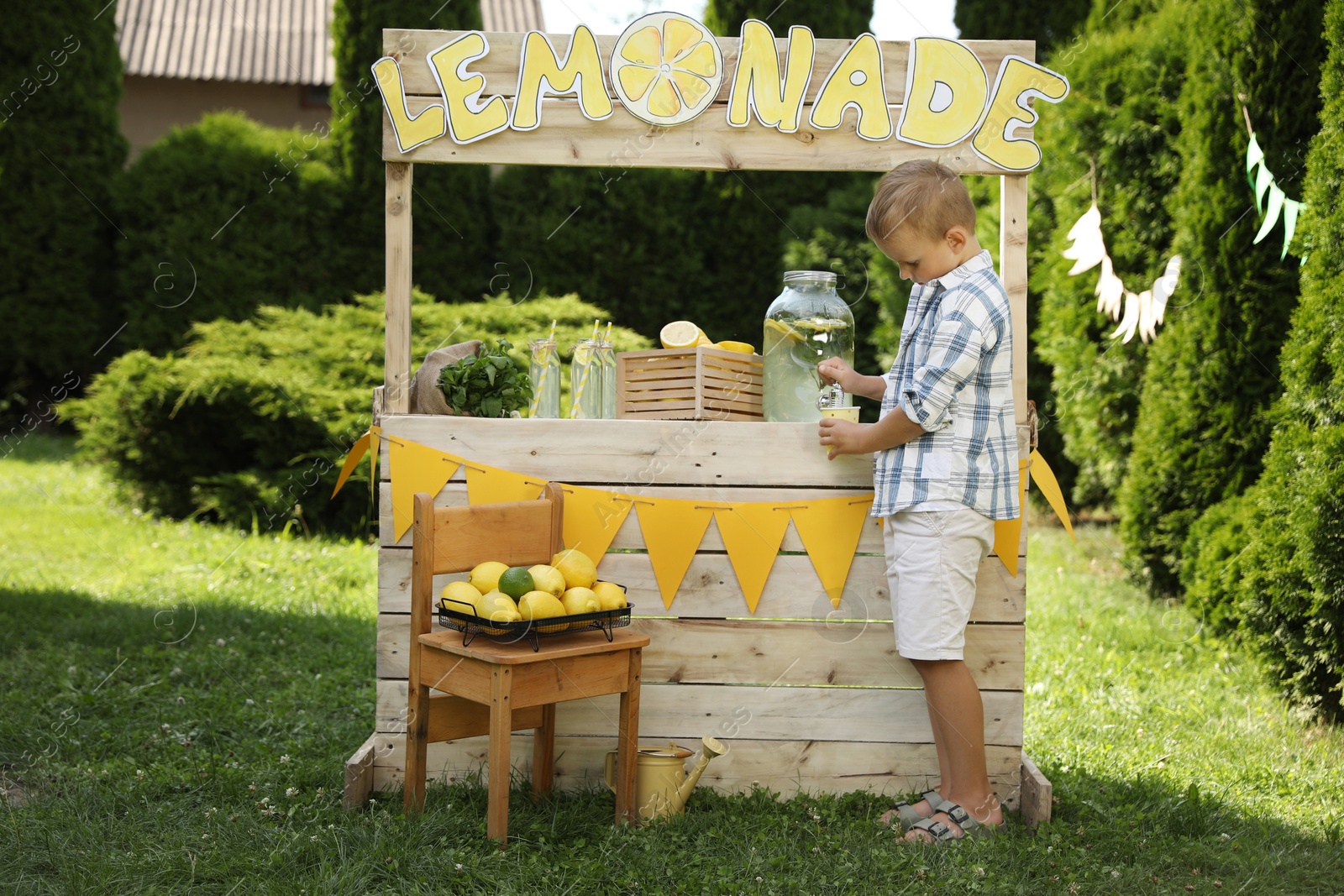 Photo of Cute boy pouring refreshing lemonade into paper cup in park