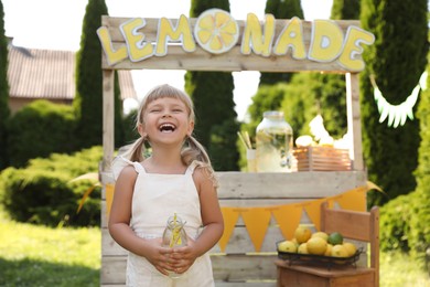 Photo of Cute little girl with refreshing drink near lemonade stand in park