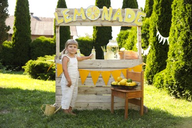 Photo of Little girl with refreshing drink near lemonade stand in park