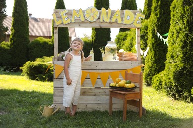 Photo of Little girl with refreshing drink near lemonade stand in park