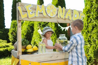 Photo of Cute little girl selling natural lemonade to boy in park