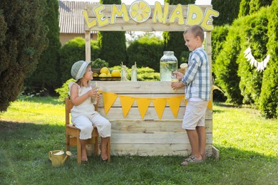 Little girl sitting on chair while boy pouring lemonade into cup in park