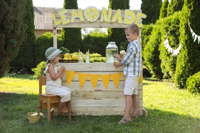 Little girl drinking beverage while boy pouring lemonade into paper cup in park