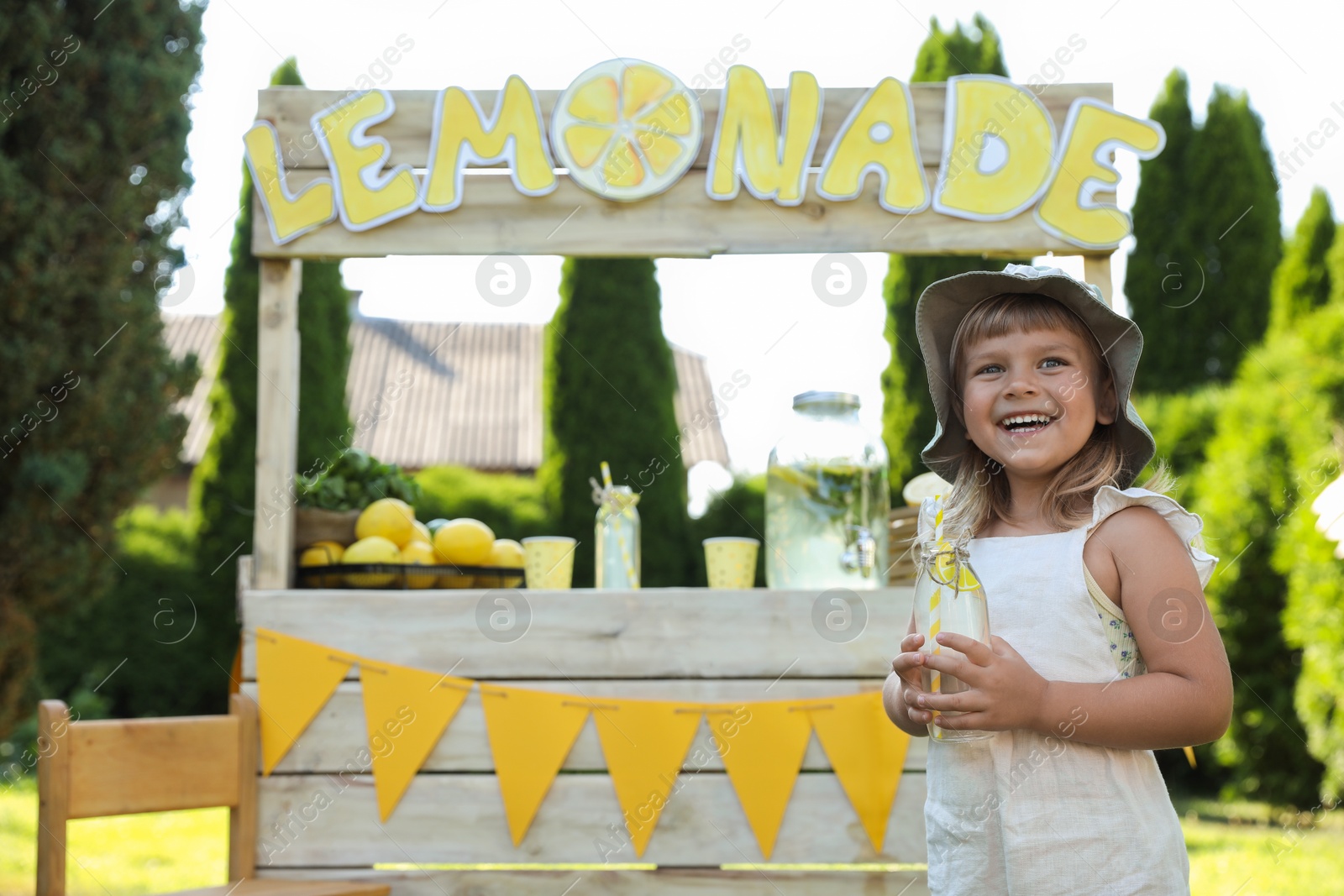 Photo of Cute little girl with refreshing drink near lemonade stand in park