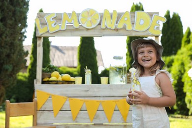 Cute little girl with refreshing drink near lemonade stand in park