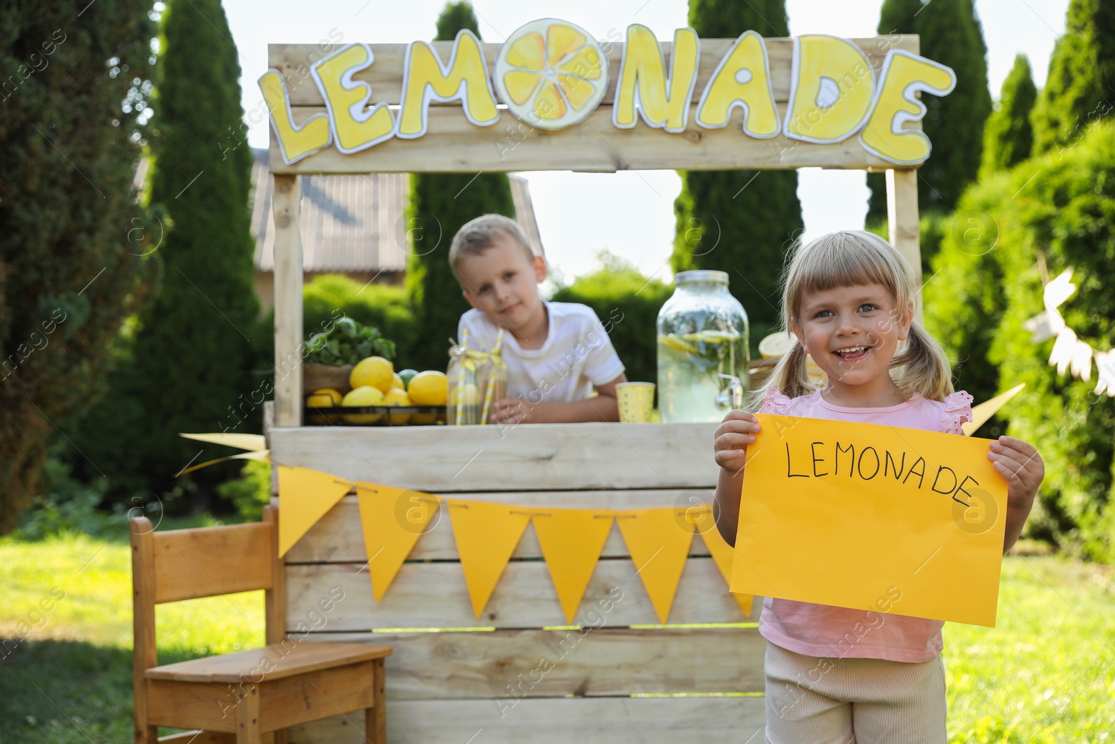 Photo of Little girl holding price tag near lemonade stand in park