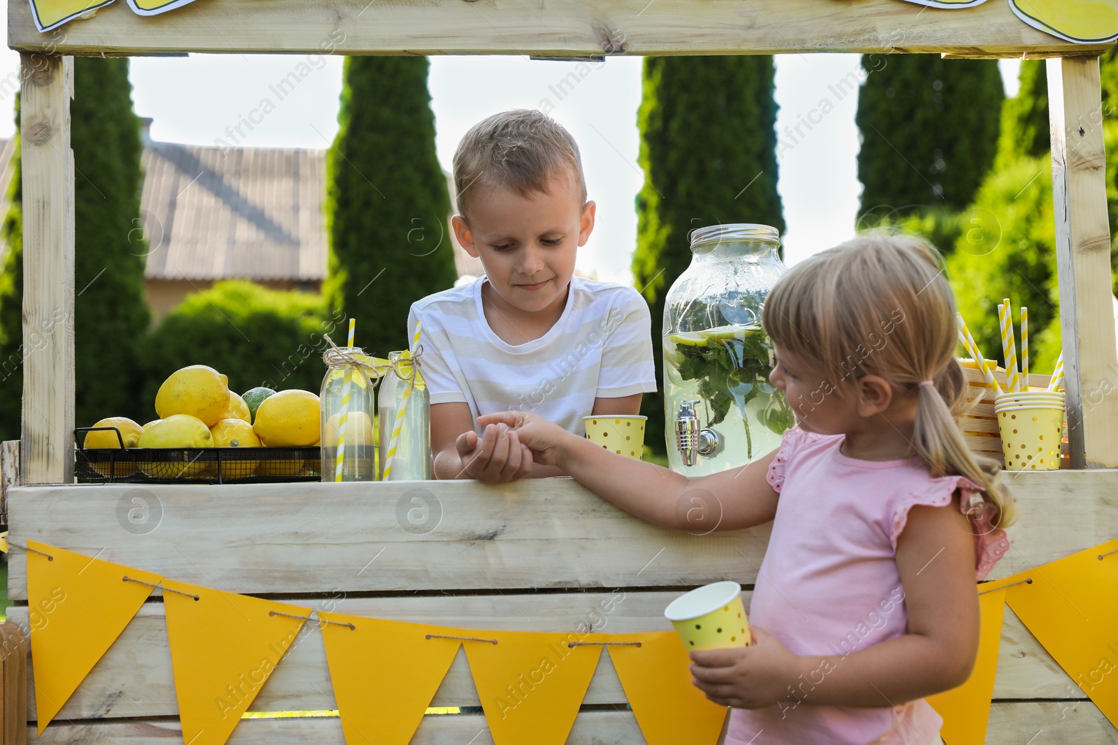 Photo of Cute little boy selling natural lemonade to girl in park