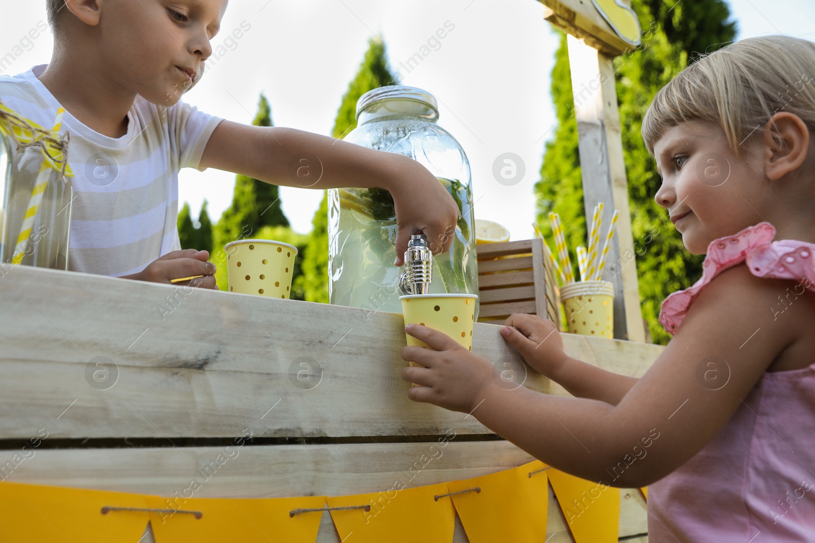 Photo of Cute boy pouring lemonade into girl's cup in park