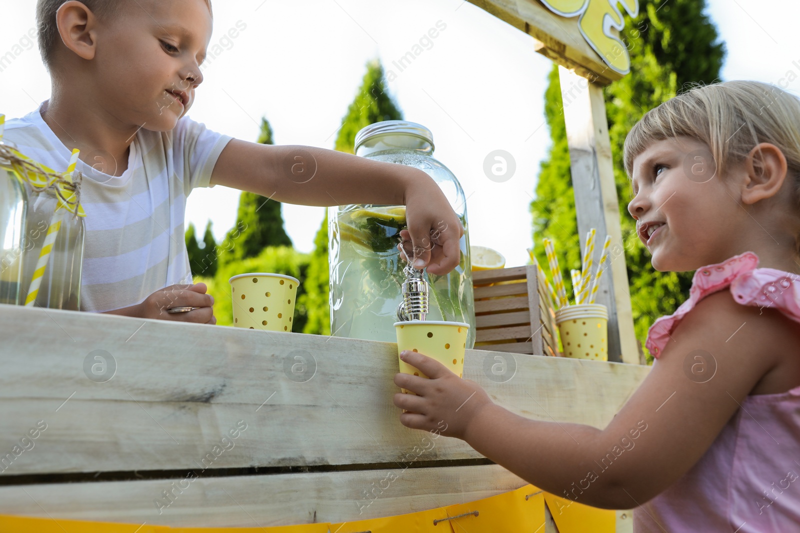 Photo of Cute boy pouring lemonade into girl's paper cup in park