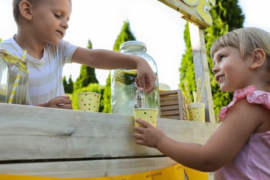 Photo of Cute boy pouring lemonade into girl's paper cup in park