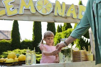 Cute little girl selling natural lemonade to woman in park