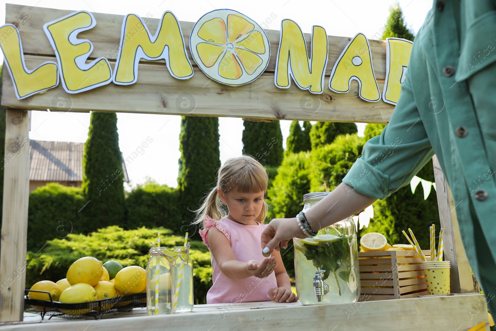 Photo of Cute little girl selling natural lemonade to woman in park