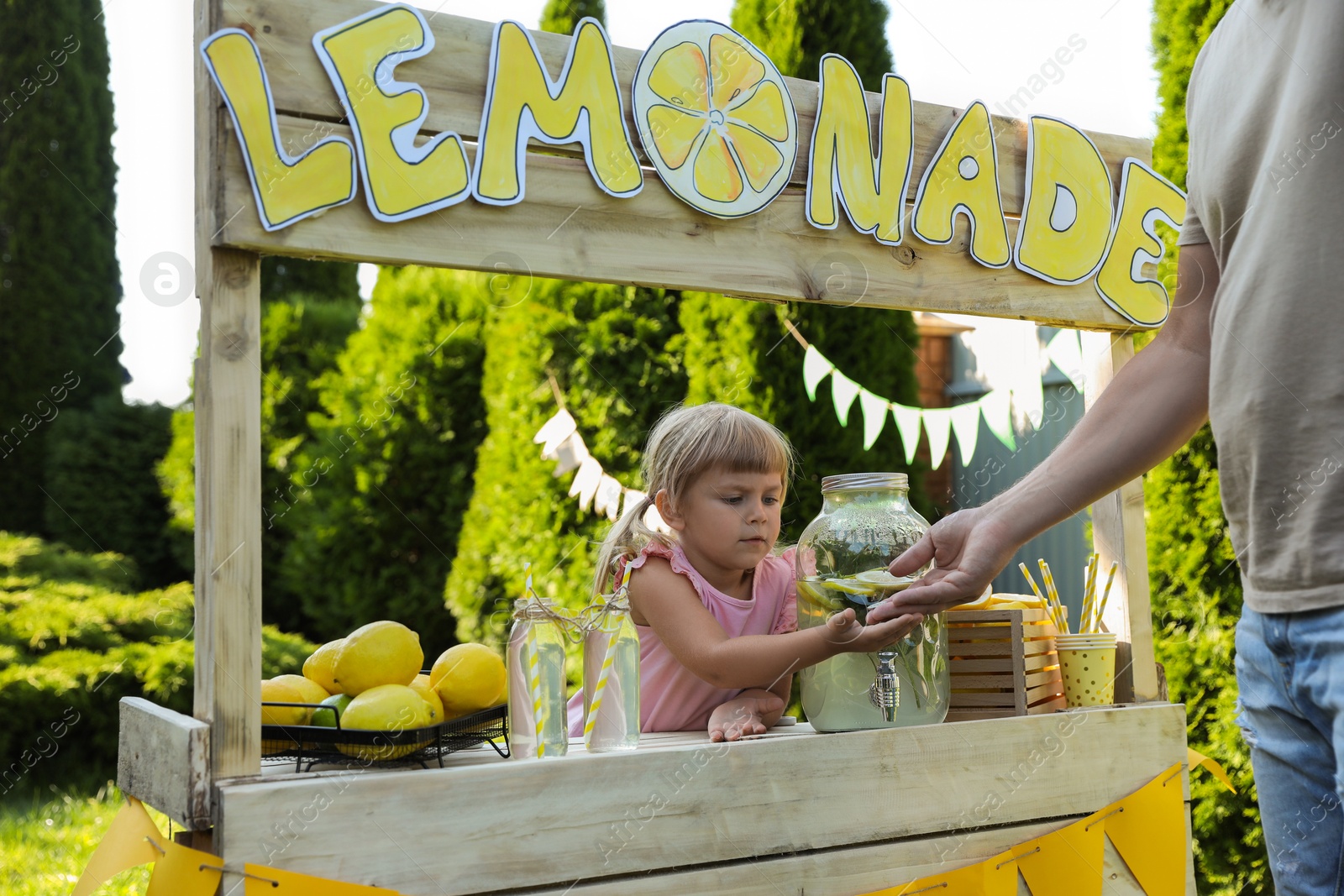 Photo of Cute little girl selling natural lemonade to man in park