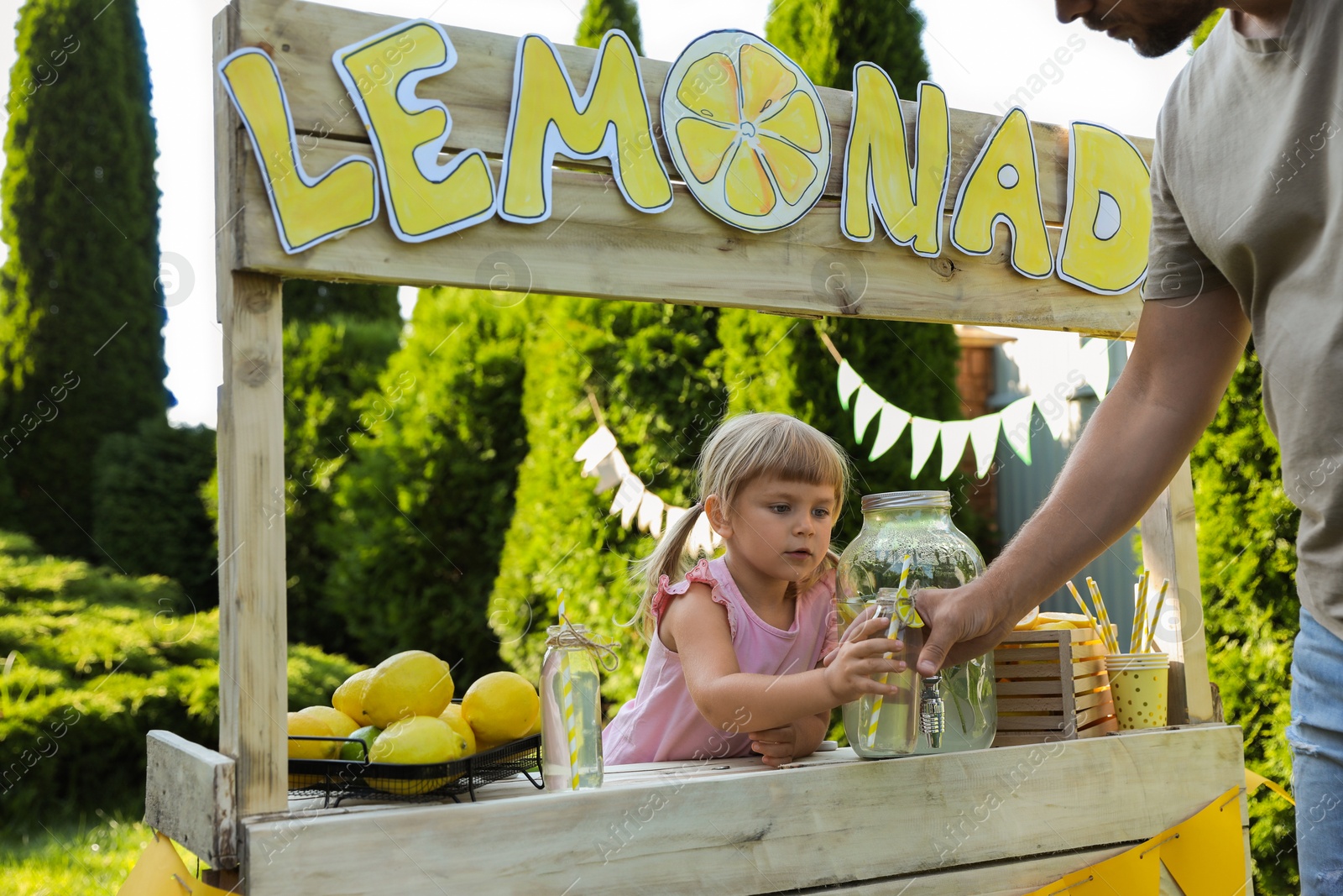 Photo of Cute little girl selling natural lemonade to man in park