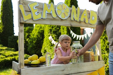 Photo of Cute little girl selling natural lemonade to man in park