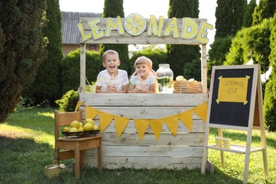 Photo of Cute little kids with refreshing drinks at lemonade stand in park