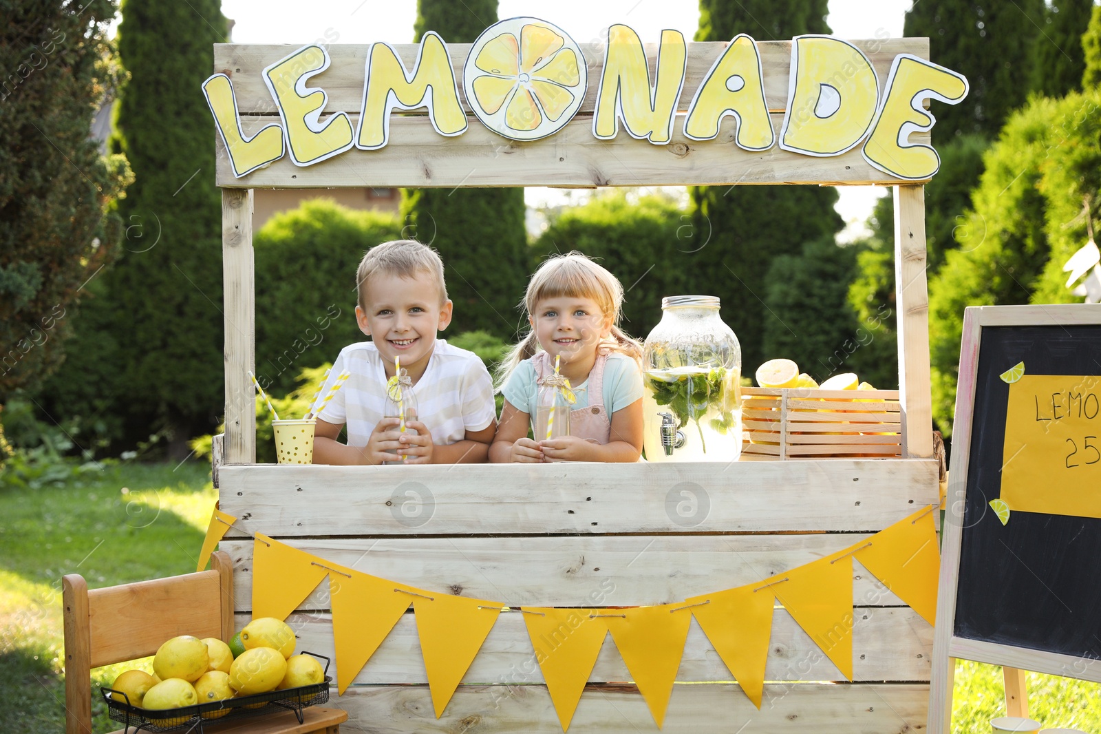 Photo of Cute little kids with refreshing drinks at lemonade stand in park