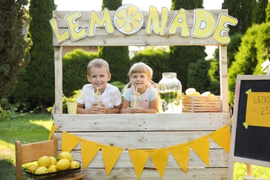 Cute little kids with refreshing drinks at lemonade stand in park