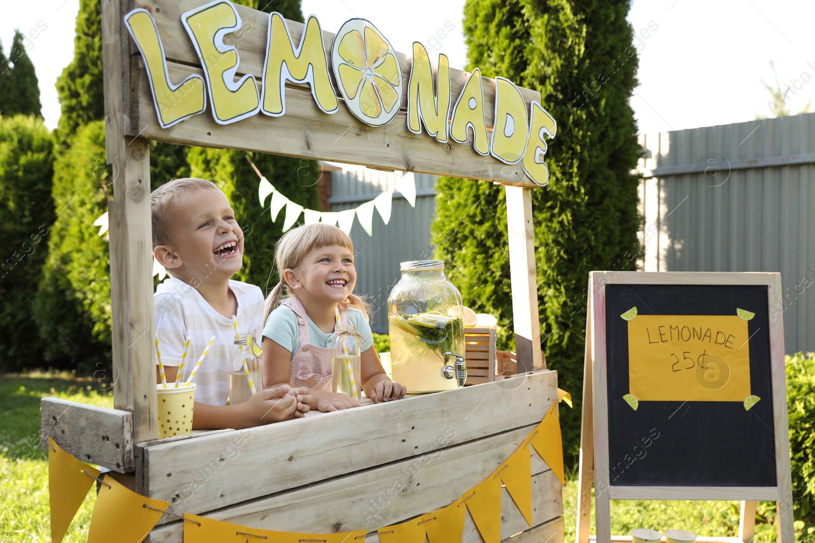 Photo of Cute little kids with refreshing drinks at lemonade stand in park