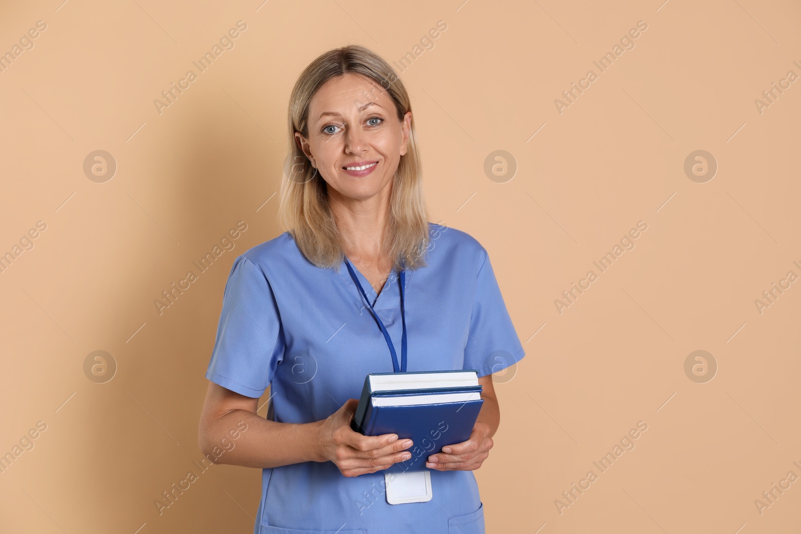 Photo of Nurse in medical uniform with badge and books on beige background