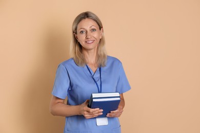 Photo of Nurse in medical uniform with badge and books on beige background