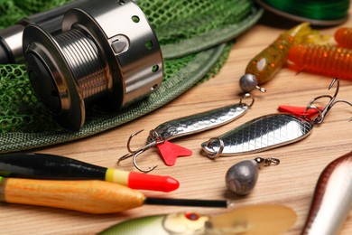 Fishing spinning reel, baits, net and floats on wooden table, closeup