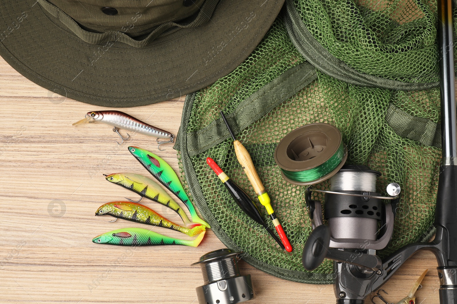 Photo of Fishing rod with spinning reel, baits, hat, net, floats and line on wooden table, top view