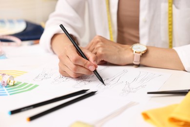 Fashion designer drawing sketch of beautiful outfit at table in workshop, closeup