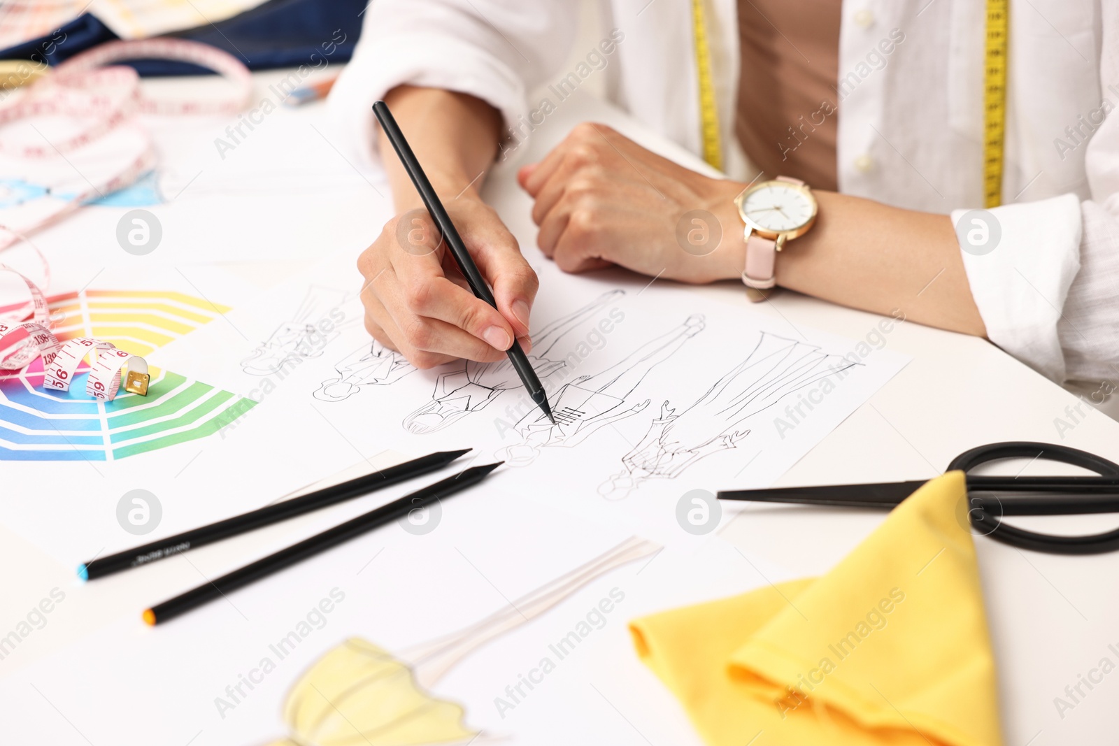 Photo of Fashion designer drawing sketch of beautiful outfit at table in workshop, closeup