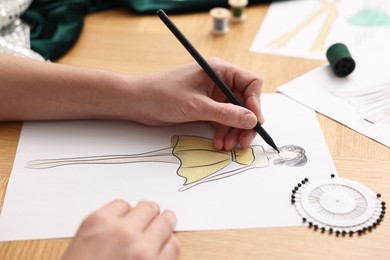 Photo of Fashion designer drawing sketch of beautiful dress at wooden table, closeup