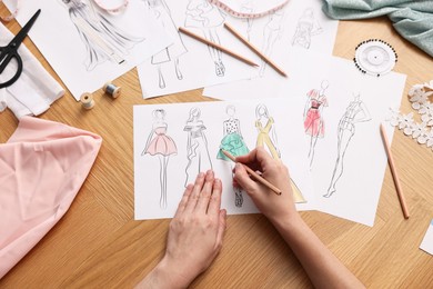 Photo of Fashion designer drawing sketch of beautiful dress at wooden table, top view