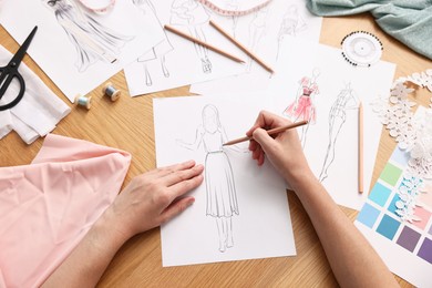 Fashion designer drawing sketch of beautiful dress at wooden table, top view