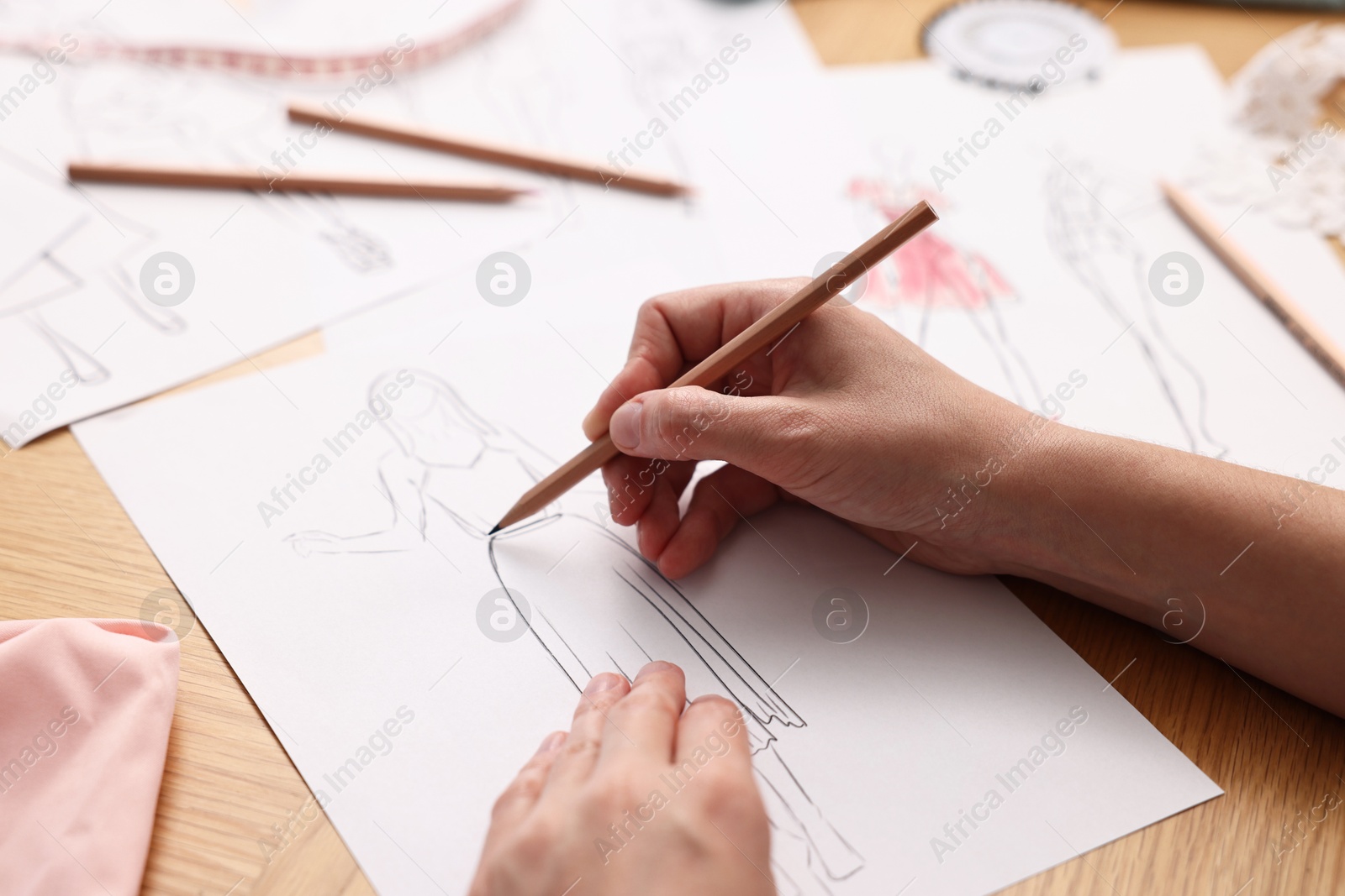 Photo of Fashion designer drawing sketch of dress at wooden table, closeup