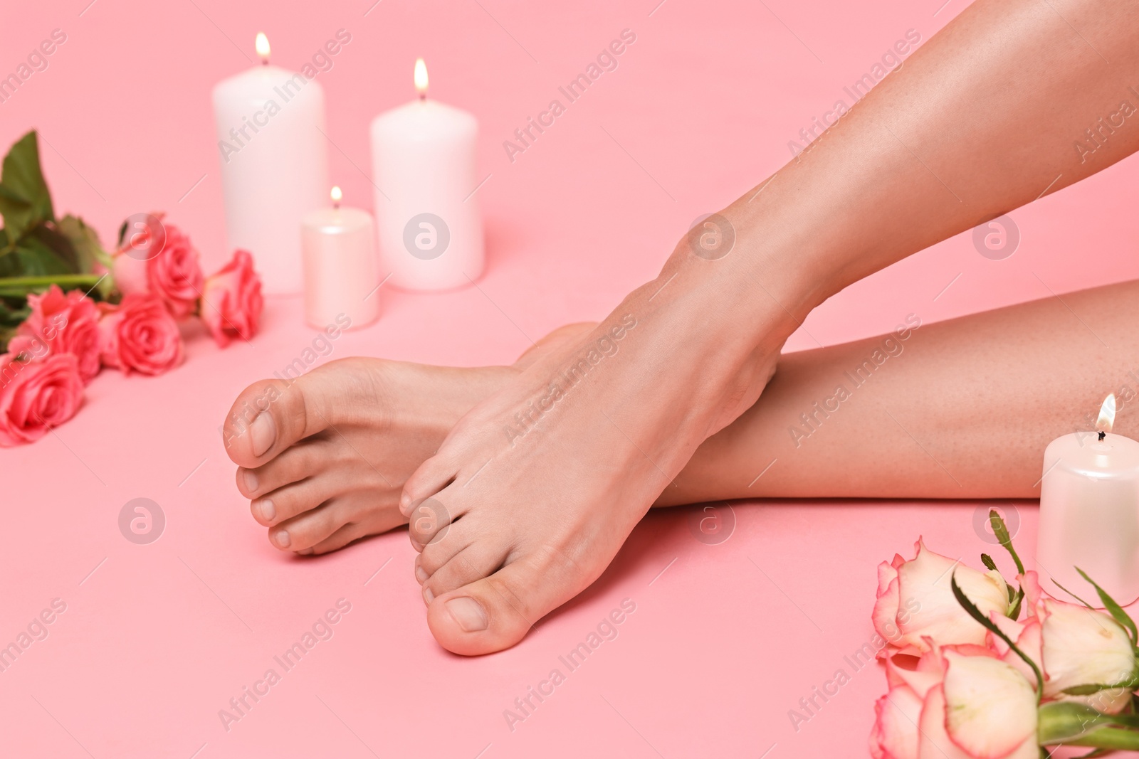 Photo of Woman with smooth feet, burning candles and roses on pink background, closeup