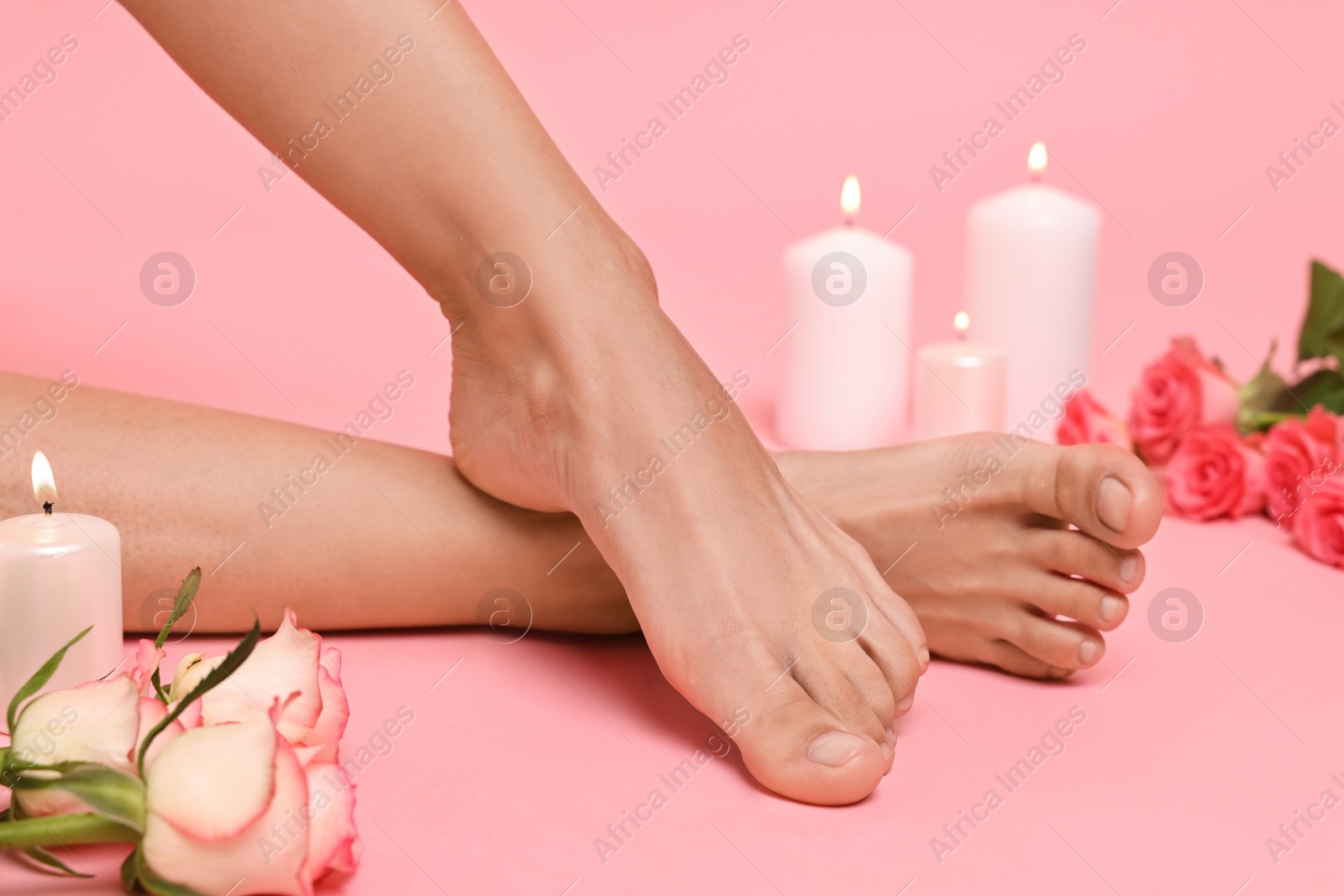 Photo of Woman with smooth feet, burning candles and roses on pink background, closeup