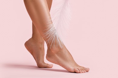 Photo of Woman with smooth feet and feather on pink background, closeup