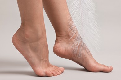 Photo of Woman with smooth feet and feather on grey background, closeup