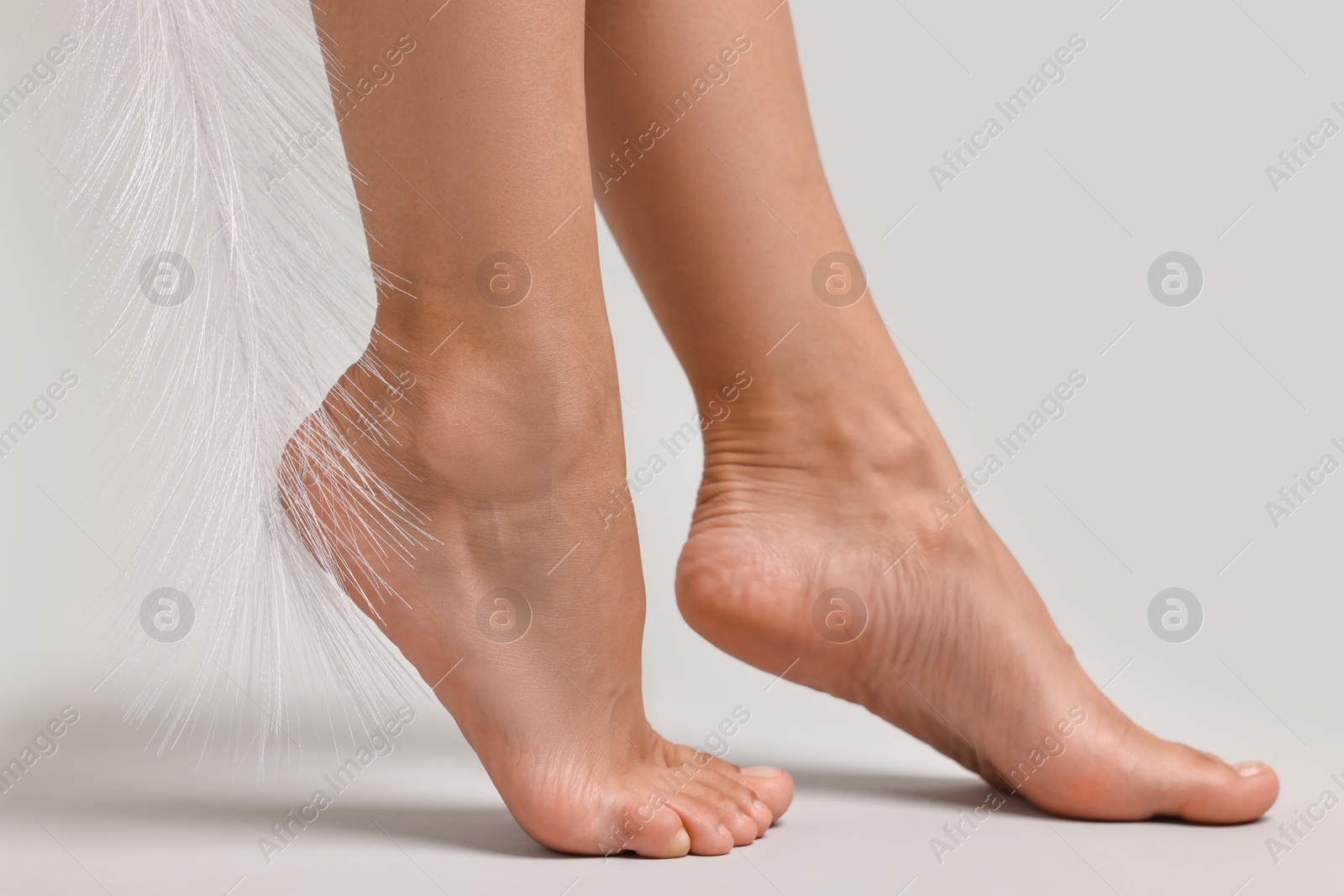 Photo of Woman with smooth feet and feather on grey background, closeup