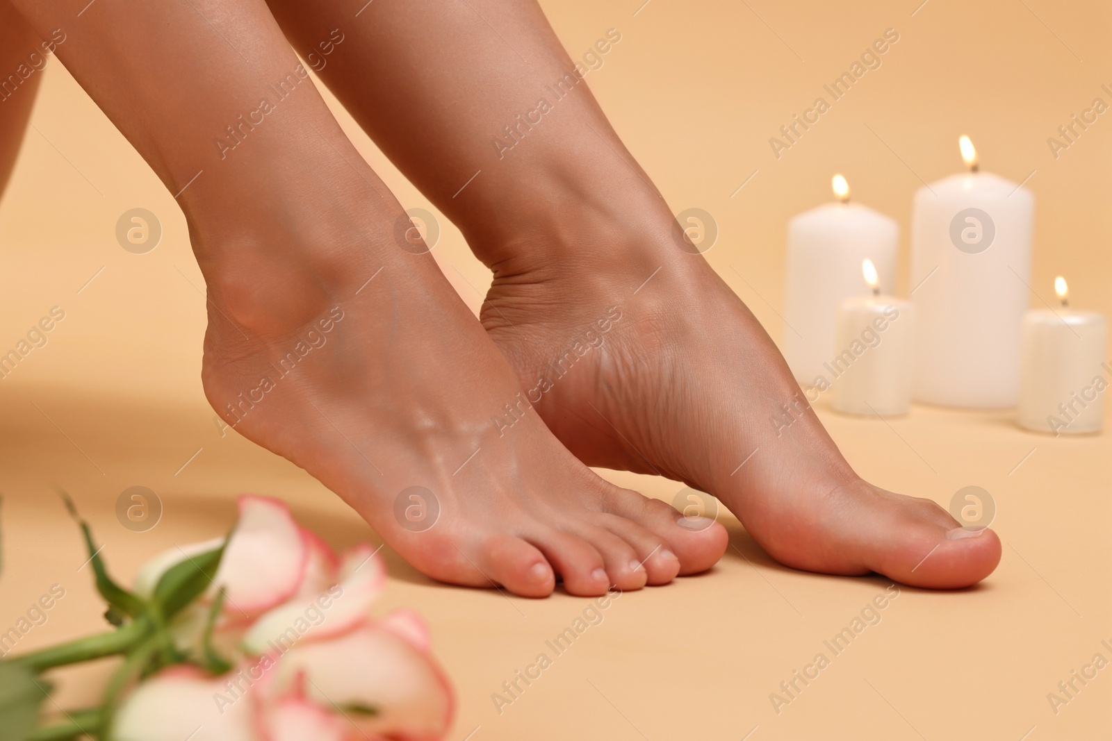 Photo of Woman with smooth feet, burning candles and roses on beige background, closeup