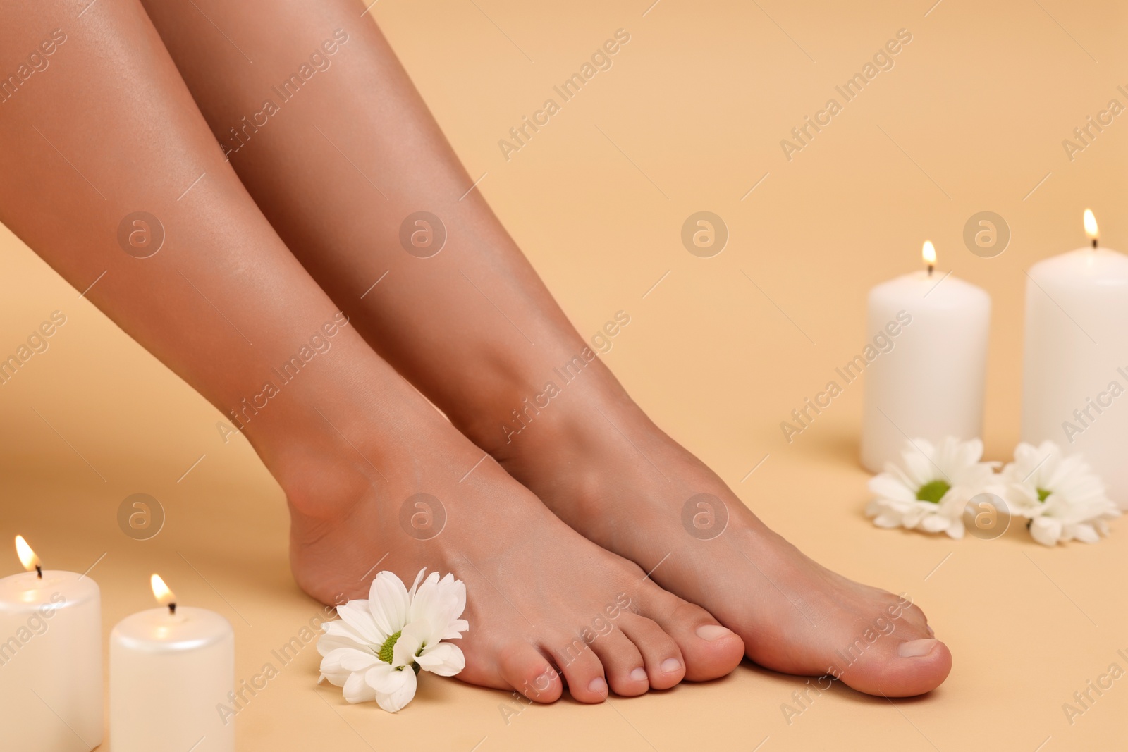 Woman with smooth feet, burning candles and chrysanthemum flowers on beige background, closeup Photo of Woman with smooth feet, burning candles and chrysanthemum flowers on beige background, closeup