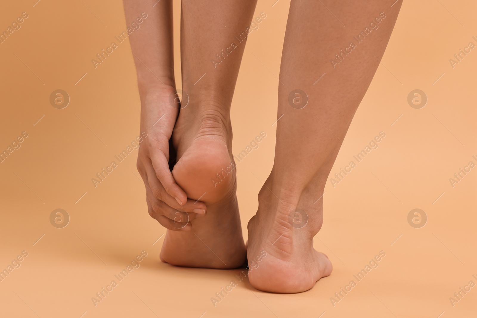 Photo of Woman touching her smooth feet on beige background, closeup