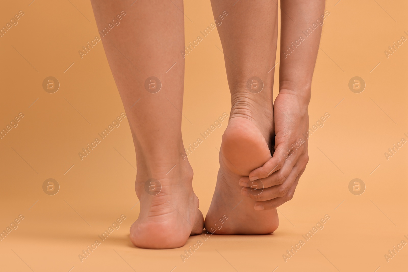 Photo of Woman touching her smooth feet on beige background, closeup