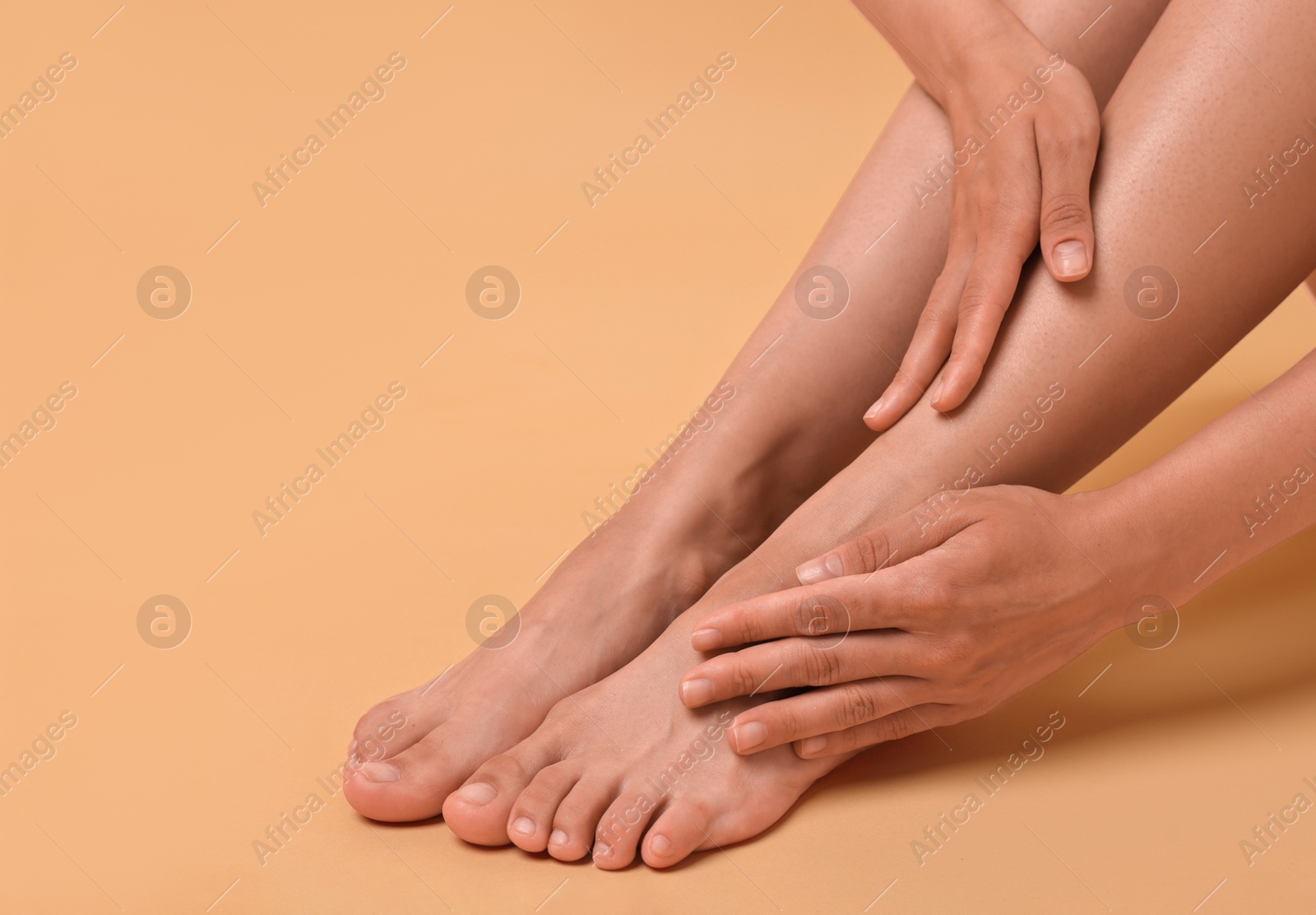 Woman touching her smooth feet on beige background, closeup Photo of Woman touching her smooth feet on beige background, closeup