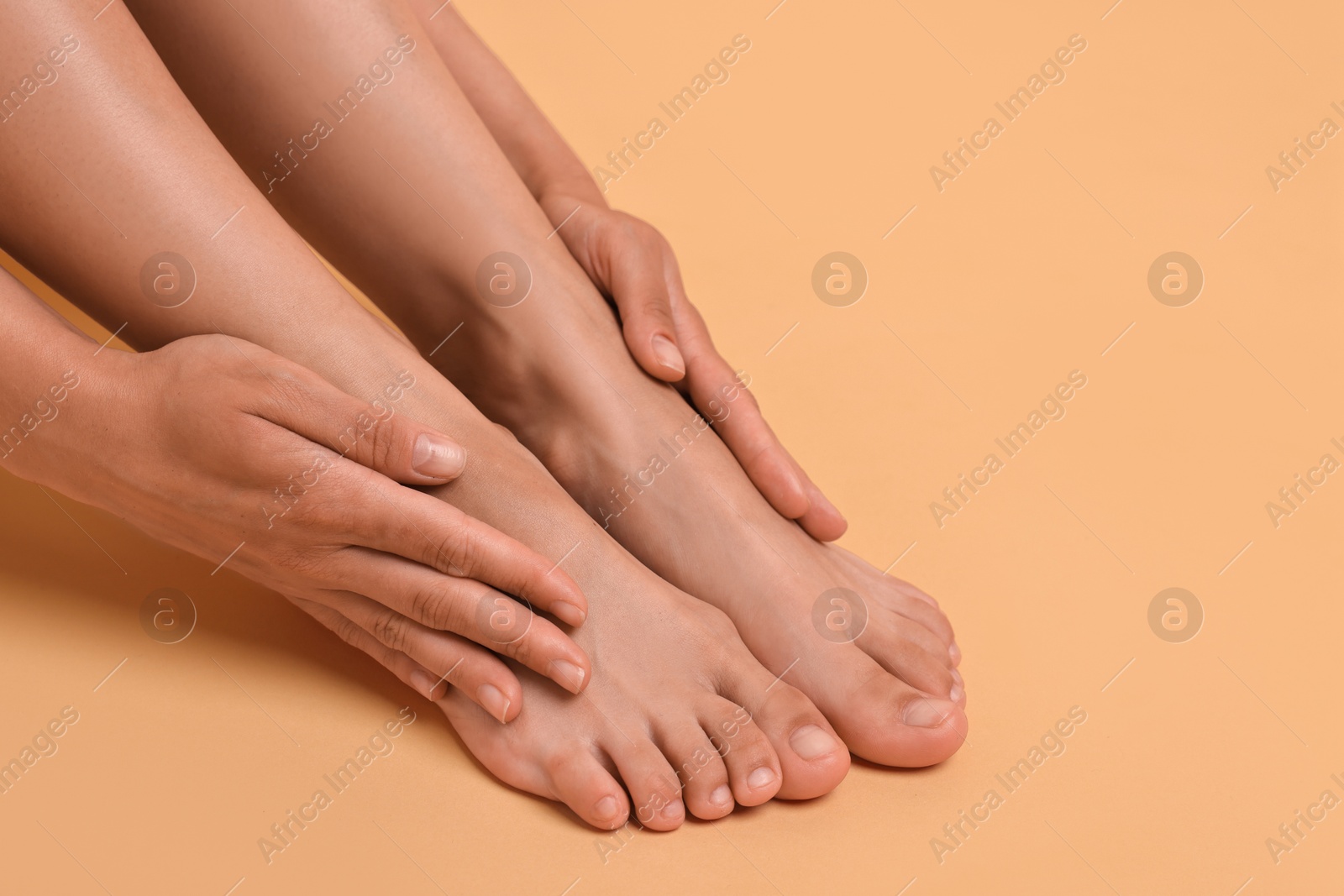 Photo of Woman touching her smooth feet on beige background, closeup